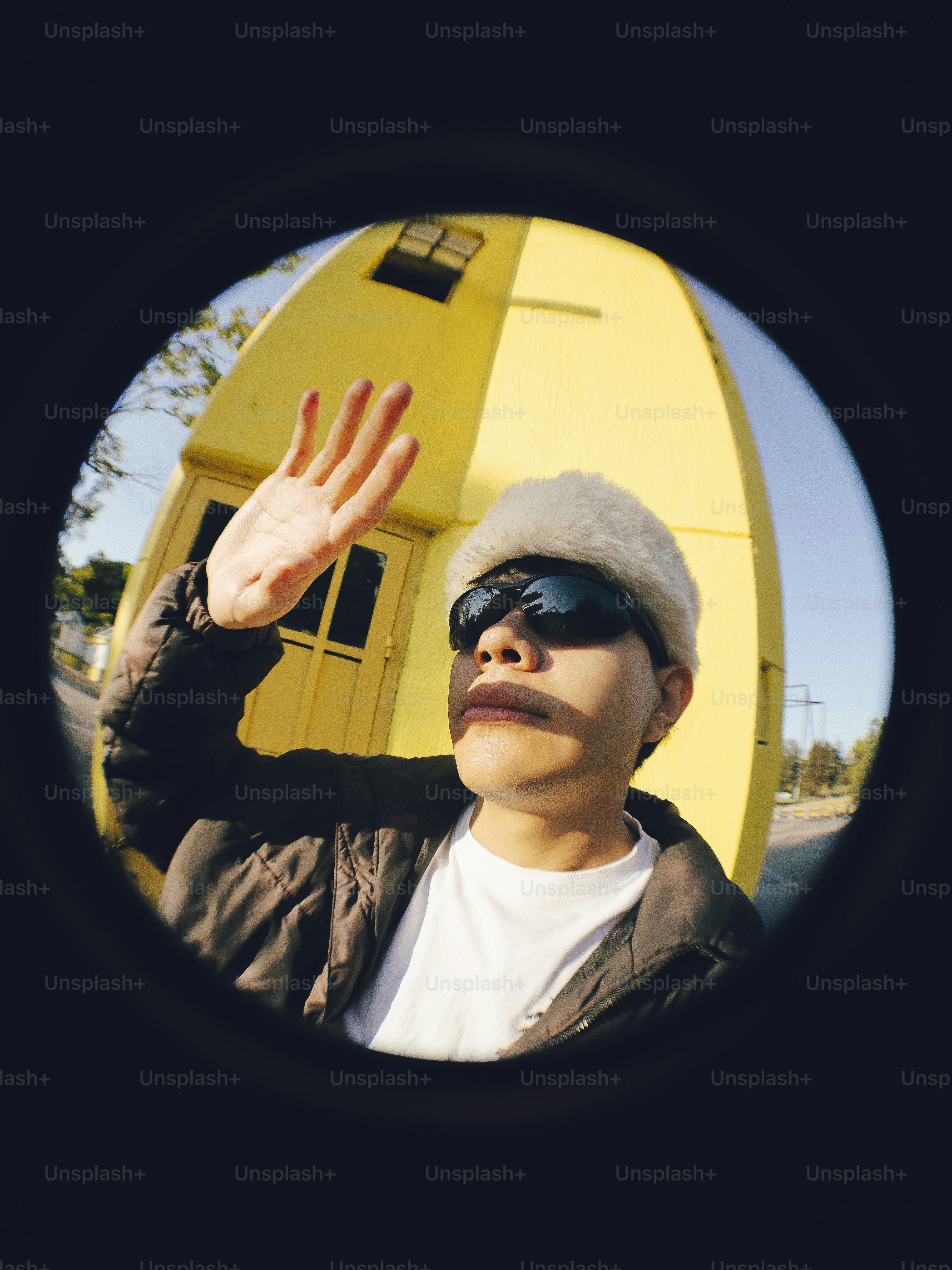 A man wearing sunglasses and a hat with his hand up in the air